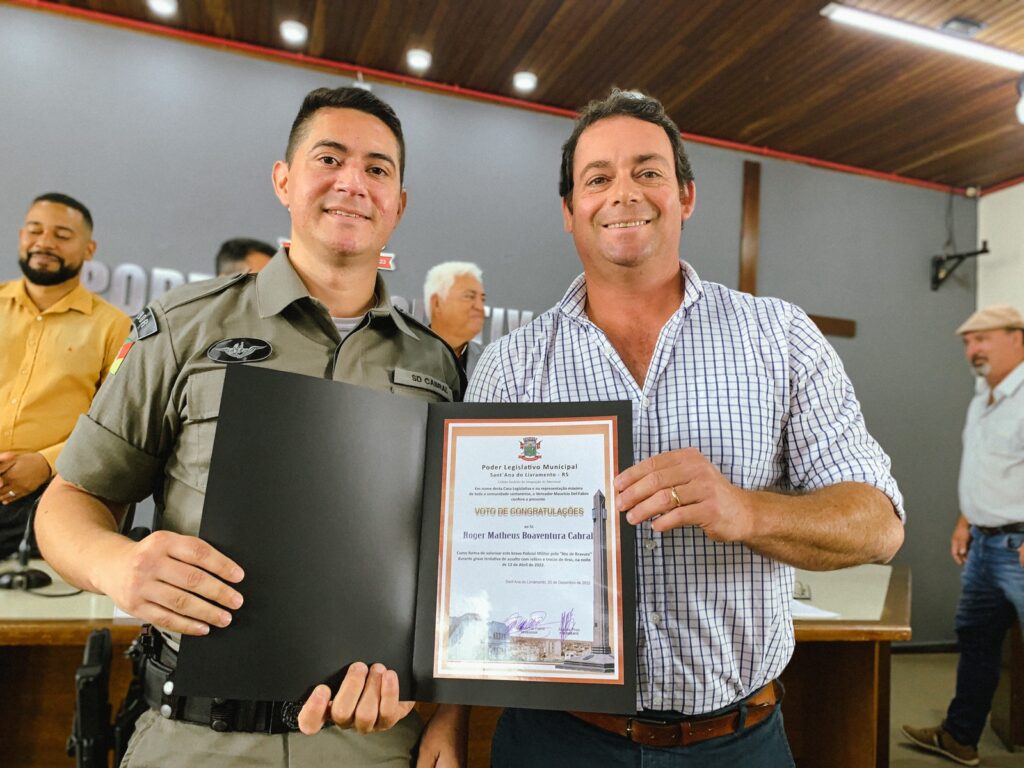 Na manhã desta terça-feira (20), o vereador Maurício Galo Del Fabro (Progressistas) fez a entrega de um Voto de Congratulação ao soldado Roger Matheus Boaventura Cabral pelo seu "Ato de Bravura" durante grave tentativa de assalto com reféns, troca de tiros e assaltante morto na noite do dia 12 de abril de 2022, em Sant’Ana do Livramento”.  Narrativa do Fato; O Sargento Dionatan que estava fazendo sua mudança pessoal visualizou que o vizinho que é empresário desta cidade chegou dirigindo sua motocicleta e adentrou a sua residência e logo atrás dele desembarcaram de um carro prata três indivíduos que adentraram a residência e o motorista do carro ficou dando voltas na quadra, estranhando o fato, pediu apoio ao soldado Cabral que estava de folga e observaram que se tratava de um roubo e acionaram o 190. O Soldado Cabral iniciou a averiguação em torno da casa, quando visualizou na janela lateral três indivíduos armados, deu voz de abordagem, dois estavam com pistolas em punho, e o outro com uma espingarda calibre .12, os quais investiram contra o soldado Cabral, efetuando disparos de arma de fogo, na intenção de cessar a injusta agressão, foram realizados disparos de arma de fogo em legitima defesa onde um dos indivíduos foi alvejado. Após o confronto o soldado Cabral e os policiais que chegaram em apoio entraram na residência e localizaram as vitimas, as quais estavam em um quarto todas amarradas com lacre e fitas na boca, isto é, com a liberdade restrita. As vitimas foram resgatadas, e as buscas pelos indiciados foram reiniciadas. Na parede da sacada do segundo piso foram visualizadas marcas de sangue em direção a uma obra do pátio vizinho em que os assaltantes pularam de uma altura superior a seis metros, onde o soldado Cabral, soldado Larrea e o sargento Emmanoel seguiram no encalço dos suspeitos. Ao adentrar neste terreno houve outro confronto, pois os indiciados atiraram contra os policiais novamente, momento em que reagiram a injusta agressão, e após os indivíduos foram rendidos cada um com uma pistola 9mm e uma mochila contendo três carregadores e munições calibre 9mm apreendidas. O SAMU foi acionado para socorrer os assaltantes que foram alvejados e precisaram do apoio dos bombeiros pois o local era de difícil acesso devido a altura.  As vitimas do sequestro foram libertadas da casa, os quais relataram que havia mais um individuo ali dentro, e foi encontrado embaixo de uma cama com uma calibre .12. Um dos assaltantes permaneceu hospitalizado sob custodia da BM, e o outro meliante veio a óbito no hospital. Foi realizada consulta e o veículo que foi usado e abandonado, foi clonado.  A delegada Giovana Muller, foi comunicada e determinou a lavratura do flagrante. O soldado Roger Matheus Boaventura Cabral, Id Func 4357817, um dos mais importantes papeis no decorrer da ocorrência pois o mesmo que estava de folga não pensou duas vezes quando foi acionado pelo sargento Dionatan para ver uma situação quase que na frente de sua casa, sobre o carro e a entrada de três indivíduos que fizeram o proprietário que chegava em casa entrar a força meio que correndo para o interior da residência, os mesmos efetuaram ligação para o CIOSP que acionou as VTR da rede CIOSP, o mesmo participou dos dois confrontos com os meliantes, sendo que enquanto aguardava apoio das guarnições de serviço confrontou pela primeira vez por uma janela lateral da casa onde alvejou um dos assaltantes e após a entrada na residência libertaram quatro pessoas da família que estavam sendo feitas reféns e posterior enfrentaram novamente a quadrilha de assaltantes logrando êxito na captura dos mesmos. 